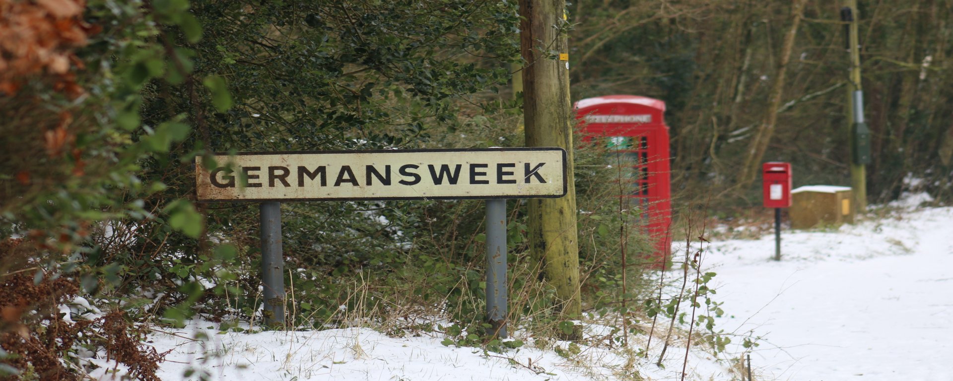 Photo of The phone box and post box in the snow behind the Germansweek village sign. 